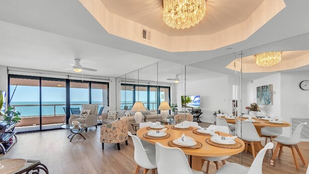 Ein modernes Wohnzimmer mit großem Esstisch, weißen Stühlen und Meerblick.