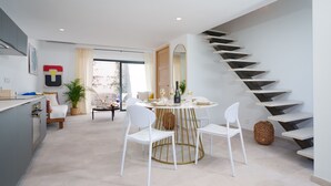 Een moderne keuken met witte kasten, een eethoek met een ronde tafel en witte stoelen, en een trap met een opvallend ontwerp.
