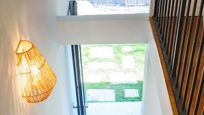 Een trap met een lamp aan de muur en uitzicht op een groen buitengebied.