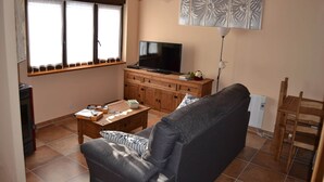 A living room with a sofa, a TV on a wooden cabinet, a coffee table, and a window with curtains. - Holiday Home in Castilla-León with Pool (Bernuy Salinero, Ávila)