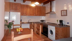 A compact kitchen with wooden cabinets, a microwave, a washing machine, and a dining area with a table and chairs. - Holiday Home in Castilla-León with Pool (Bernuy Salinero, Ávila)
