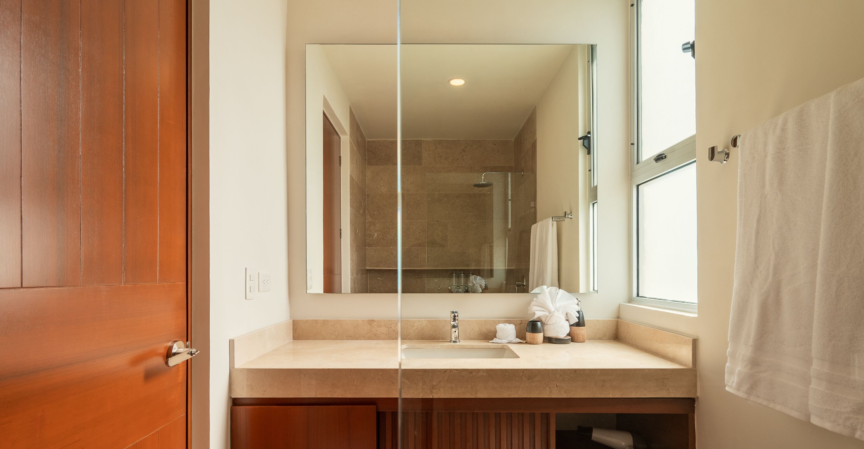 Un baño con puerta de madera, lavamanos con espejo y zona de ducha.