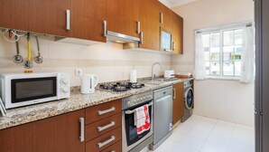 Una cocina moderna con armarios de madera, electrodomésticos de acero inoxidable, horno empotrado y una ventana con cortinas.