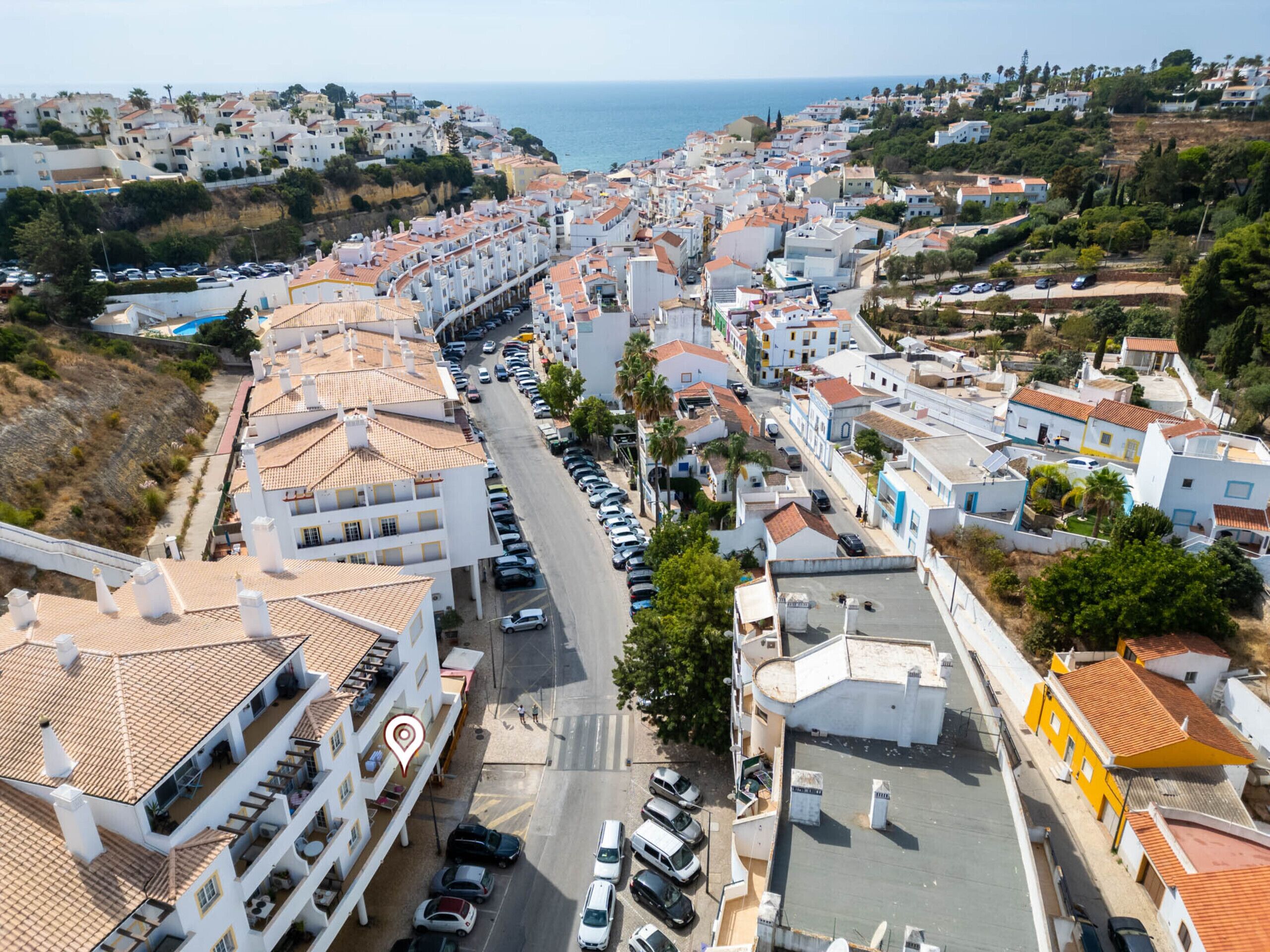Une ville côtière aux bâtiments blancs, avec une rue principale et des voitures garées.