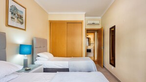 Habitación de hotel con dos camas, una mesita de noche con lámpara, un armario de madera y un cuadro en la pared.