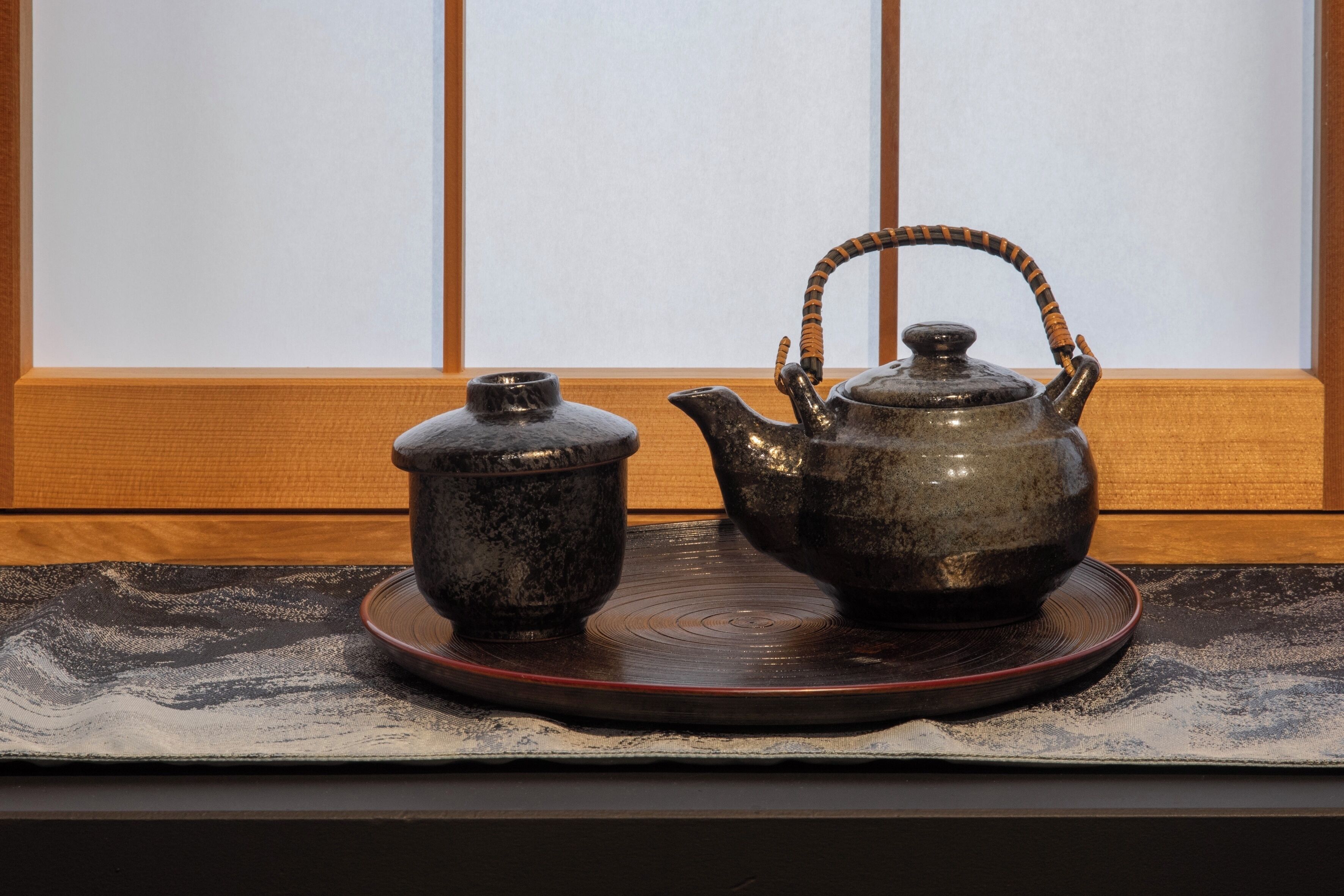 A traditional tea set with a teapot and a cup on a tray, placed on a table with a wooden panel background.