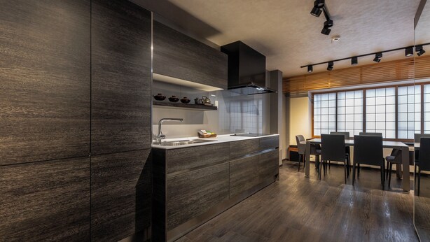 Una cocina moderna con armarios de madera oscura, una isla integrada con un lavamanos y un comedor con un amplio ventanal.