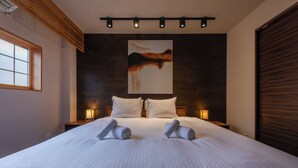 Una cama bien hecha con dos toallas enrolladas, un cuadro grande en la pared y dos lámparas de noche.