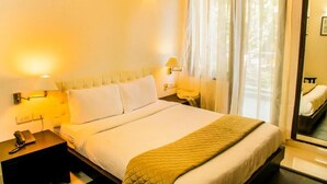 A hotel room with a large bed, bedside lamps, a nightstand with a phone, and a window with sheer curtains. - Hotel IP Swarn Near Anand Vihar Vaishali (Ghaziabad)