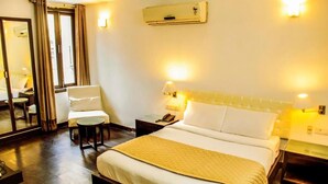 A hotel room with a bed, bedside lamps, a chair, a small table, and a mirror. - Hotel IP Swarn Near Anand Vihar Vaishali (Ghaziabad)