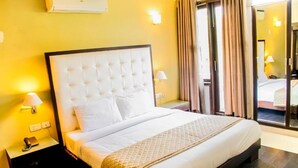 A hotel room with a large bed, a nightstand with a lamp, and a view through a glass door. - Hotel IP Swarn Near Anand Vihar Vaishali (Ghaziabad)