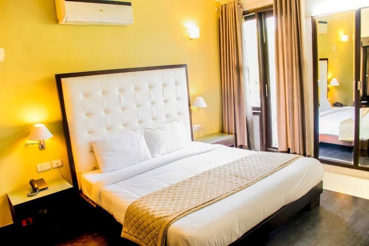 A hotel room with a large bed, a nightstand with a lamp, and a view through a glass door.