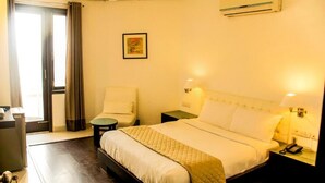 A hotel room with a bed, two chairs, a desk, a telephone, and an air conditioning unit. - Hotel IP Swarn Near Anand Vihar Vaishali (Ghaziabad)