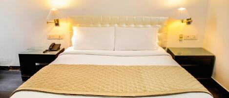 Una cama bien hecha con un edredón acolchado, dos lámparas de noche y un teléfono en la mesita.