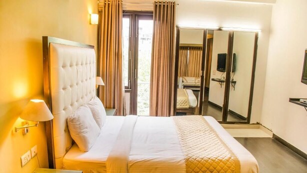 A hotel room with a large bed, a bedside telephone, a desk with a lamp, and a mirror. - Hotel IP Swarn Near Anand Vihar Vaishali (Ghaziabad)