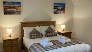 A bedroom with a wooden bed, two nightstands, a checkered bedspread, and two wall-mounted lamps. - Sherrabeg Cottage -  a cottage that sleeps 8 guests in 4 bedrooms (Laggan)