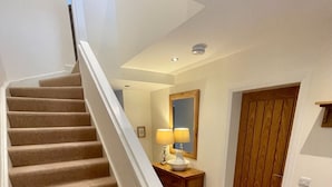 A staircase with beige carpet and white handrails leading to a landing with a wooden floor, a mirror, and a lamp. - Sherrabeg Cottage -  a cottage that sleeps 8 guests in 4 bedrooms (Laggan)
