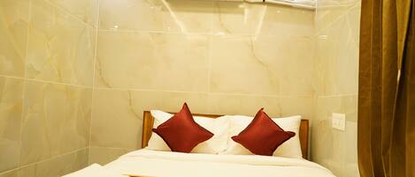 A hotel room with a bed, a wall-mounted air conditioner, and a window with curtains.