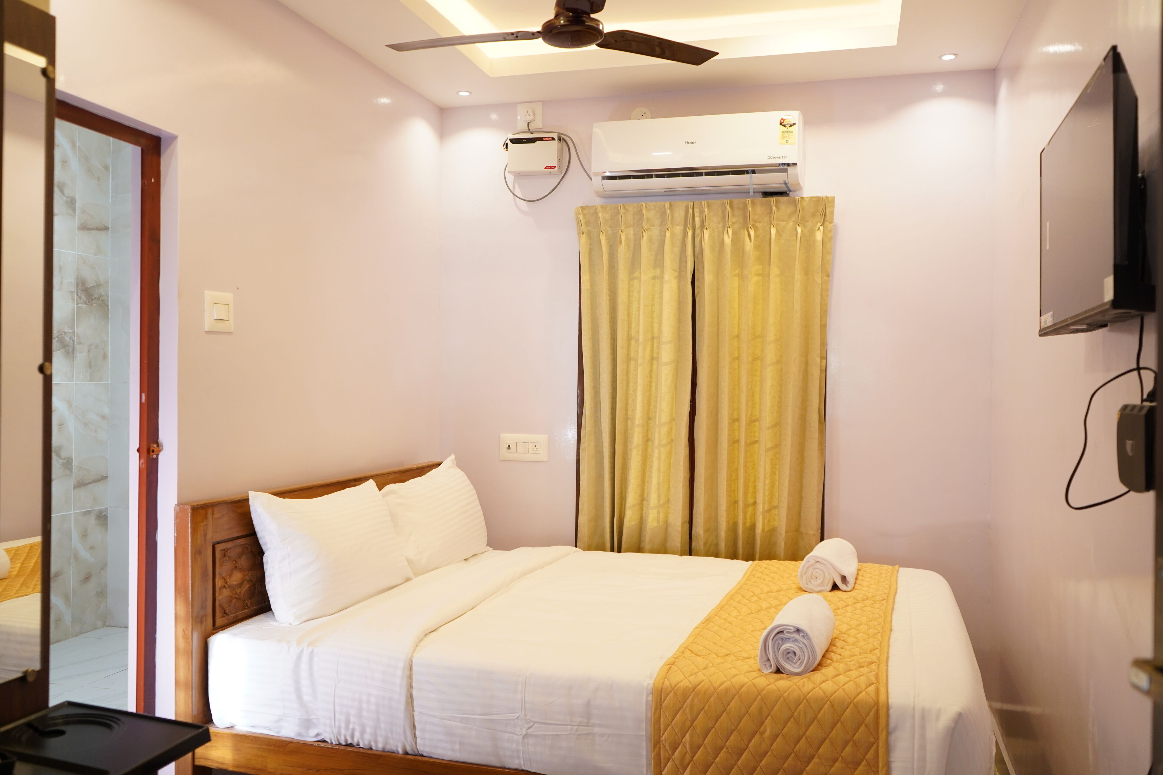 A hotel room with a bed, a ceiling fan, an air conditioning unit, a television, and a window with curtains.