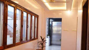 A hallway with wooden-framed windows, a ceiling fan, and a potted plant. - Golden Dawn Residency (Tiruvannamalai)