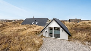 A small, modern house with a sloped roof, a gravel driveway, and a number '24' on the side.