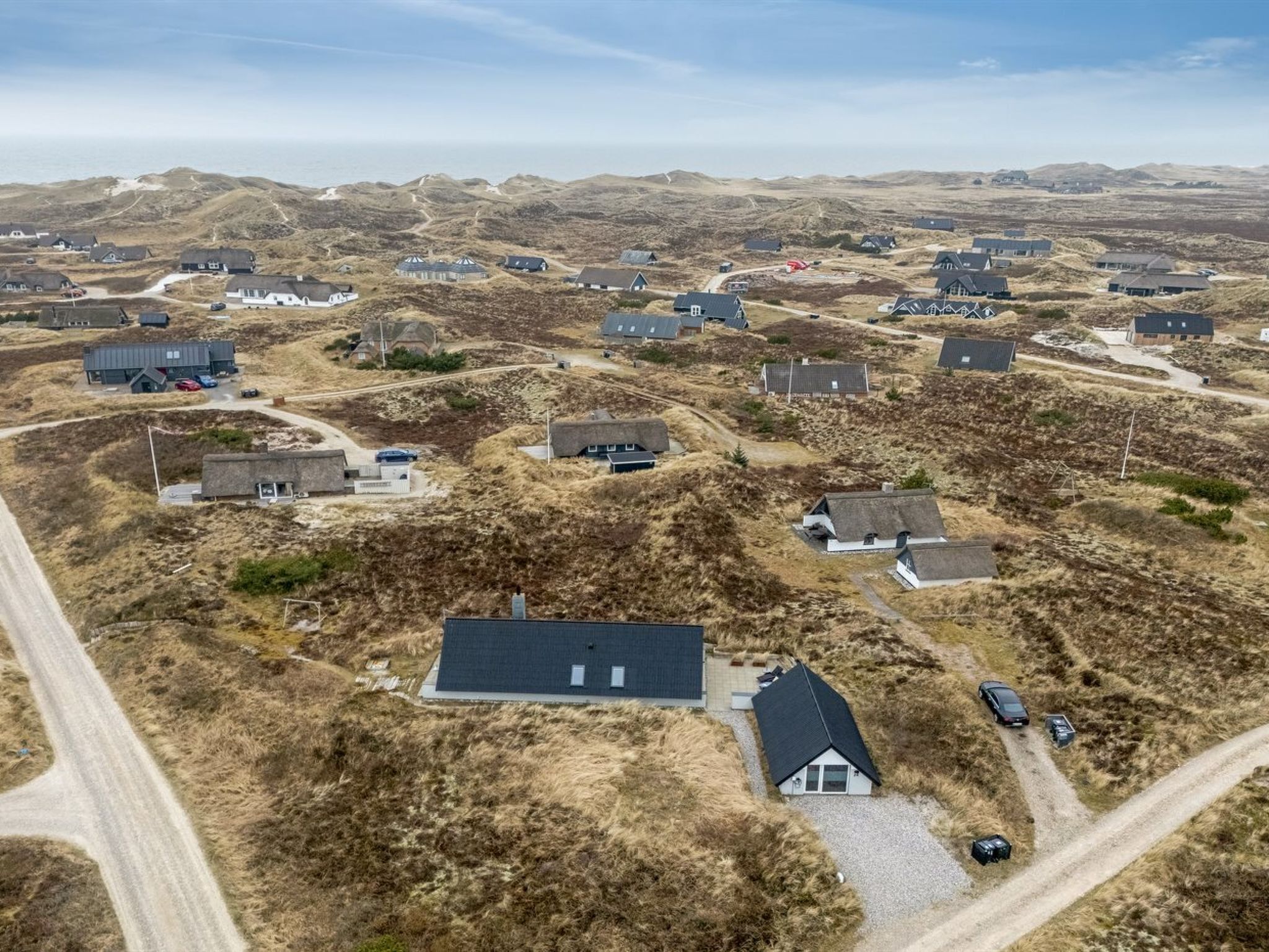 An aerial view of a residential area with houses, roads, and a beach in the background.