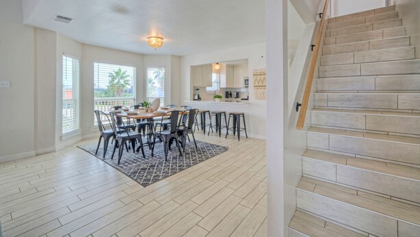 A spacious dining area with a wooden table and chairs, a patterned rug, and a staircase with wooden steps. - Sleeps 20! 2 Homes Near the Beach, Private Pools, GameRoom, Large Family Retreat (Port Aransas)