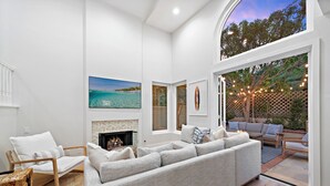 A modern living room with a large sectional sofa, a fireplace, and a view of the outdoors. - Backyard Oasis w/ Fire Table + Walk to Salt Creek Beach | Dana Point Dreams (Dana Point)