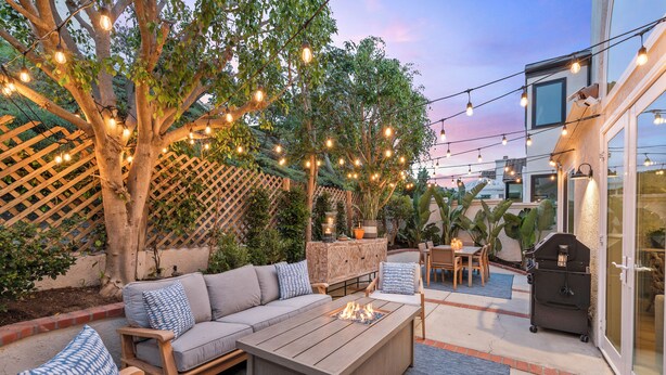 An outdoor patio with a wooden sofa, a fire pit, string lights, and a grill. - Backyard Oasis w/ Fire Table + Walk to Salt Creek Beach | Dana Point Dreams (Dana Point)