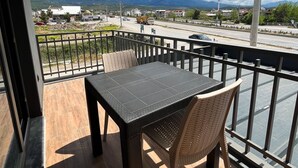 Varanda com mesa e cadeiras, vista para uma estrada com veículos e montanhas ao longe.