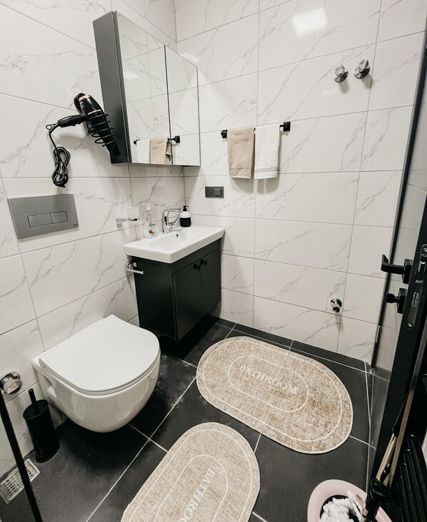 A modern bathroom with a toilet, sink, and mirror. There are two towels hanging on hooks and a shower door visible.