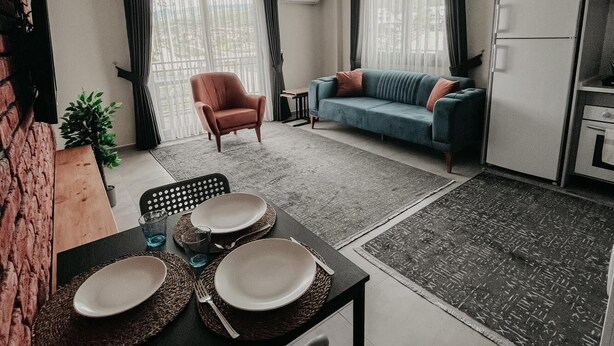 Uma sala de estar moderna com área de jantar, um sofá, uma poltrona e cozinha equipada com geladeira.