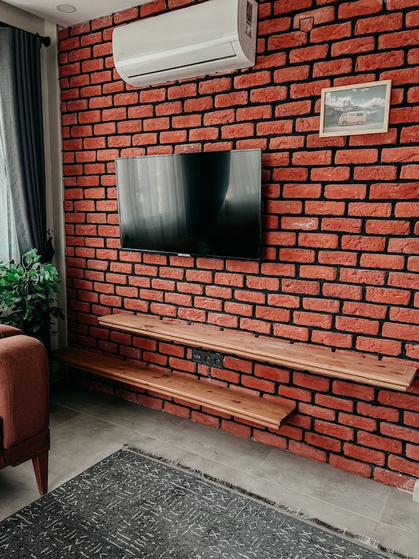 A living room with a brick wall, a mounted TV, a wooden bench, and a potted plant.