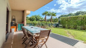 Un patio con una mesa y sillas, una pequeña cocina y vistas a un jardín con palmeras.