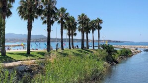 A coastal scene with palm trees, a body of water, and a distant view of mountains. - Six-Fours getaway - Beach, terrace & parking (Six-Fours-les-Plages)