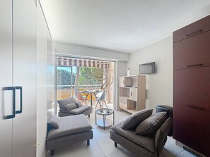 A modern living room with two grey armchairs, a small round table, a bookshelf, and a TV mounted on the wall.
