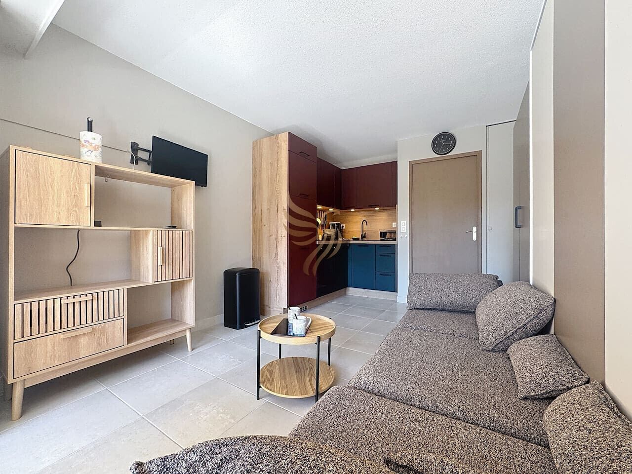 A modern living room with a sofa, a wooden cabinet, a small round table, and a kitchen area in the background.