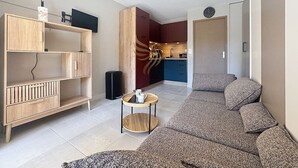 A modern living room with a sofa, a wooden cabinet, a small round table, and a kitchen area in the background. - Studio Coco`B, 4p, A/C, Wi-Fi, beach 500m, parking (Fréjus)