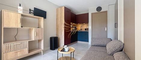 A modern living room with a sofa, a wooden cabinet, a small round table, and a kitchen area in the background.