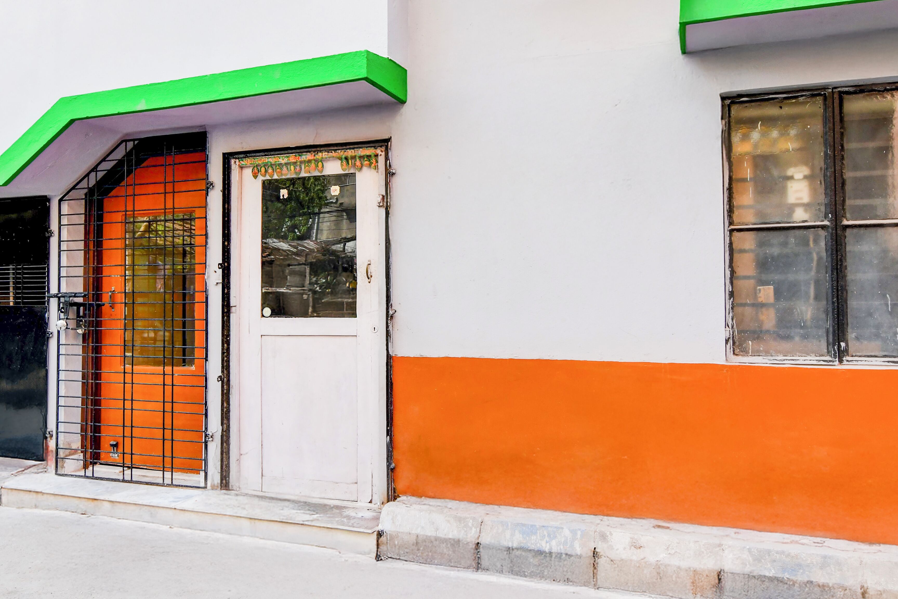 Ein Gebäude mit einer weiß-orangenen Fassade, einem grünen Dach und einem Metallgitter.