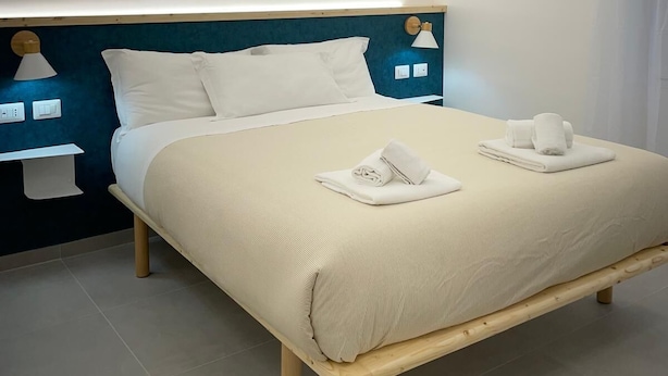 A modern hotel room with a large bed, wooden headboard, bedside tables with lamps, and neatly folded towels. - Charming double room in lovely Roma with WiFi, AC (Roma)
