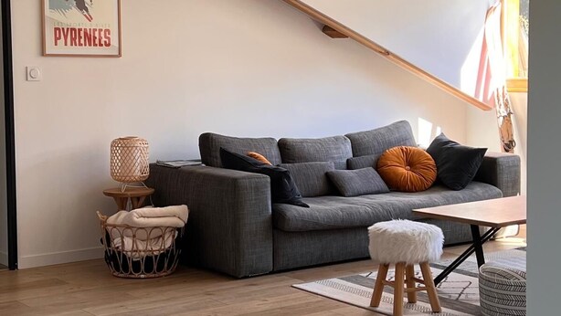 A modern living room with a grey sectional sofa, a small round table, and a wicker chair. - Lovely, warm, fully renovated apartment in the center of the village (Ax-les-Thermes)
