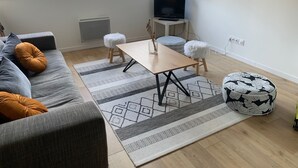A modern living room with a sofa, ottoman, and a TV on a stand. - Lovely, warm, fully renovated apartment in the center of the village (Ax-les-Thermes)