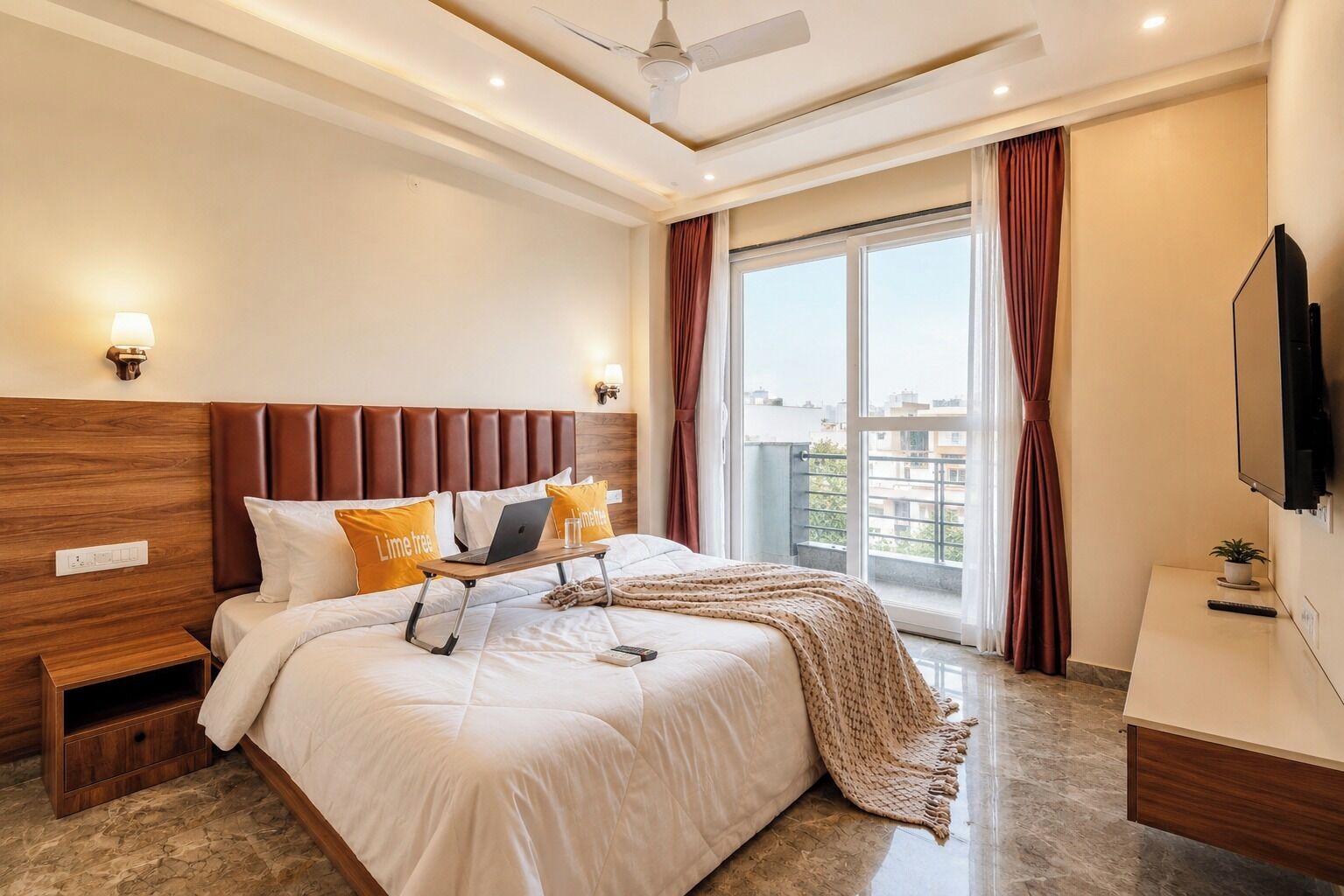 Een moderne hotelkamer met een groot bed, een bureau, een plafondventilator en een groot raam met gordijnen.