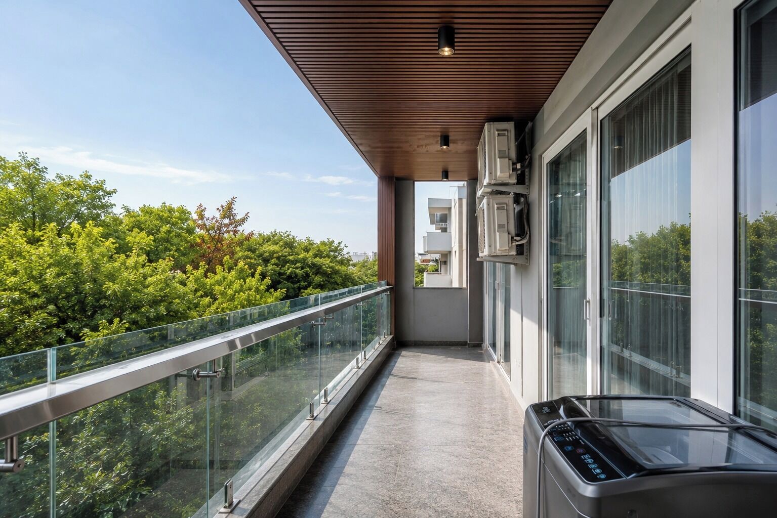 A balcony with a glass railing, air conditioning units, and a view of greenery.