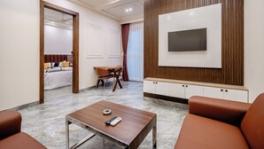 Une chambre d’hôtel moderne dotée d’un téléviseur à écran plat fixé au mur, d’un mur d’accent en bois, d’un sol en marbre, d’un lit avec une literie blanche, d’une table à manger avec des chaises et d’une table basse avec une télécommande.