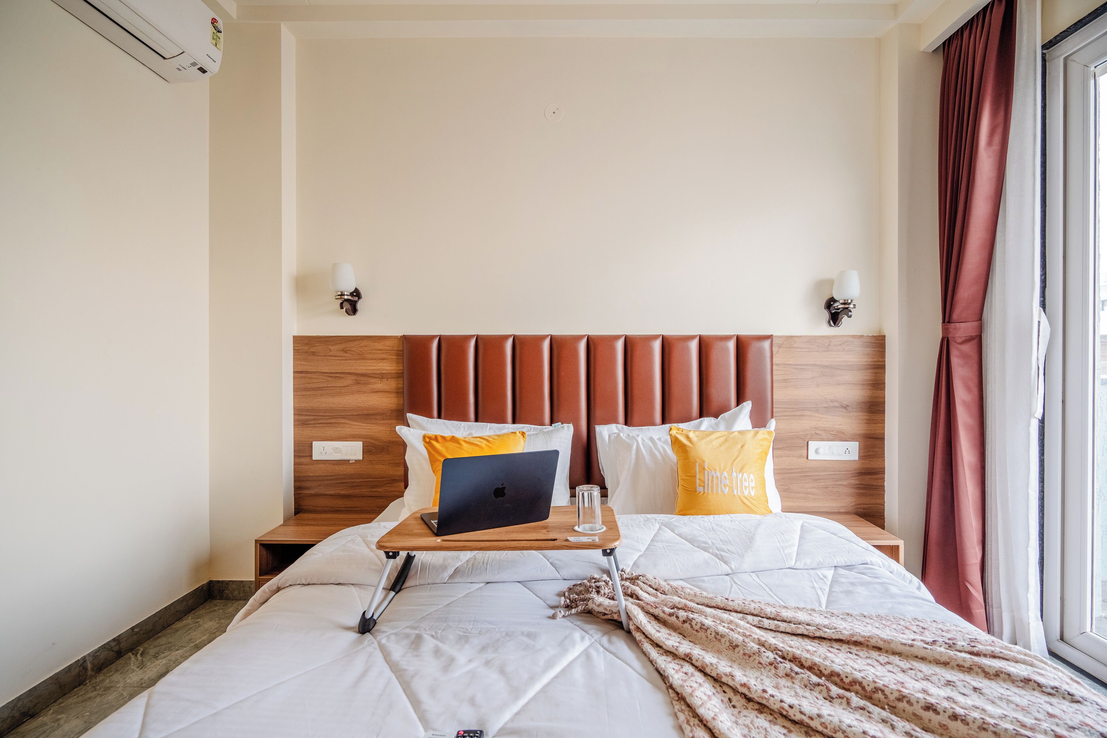 A hotel room with a bed, a laptop on a tray, and a bedside table with a glass of water.