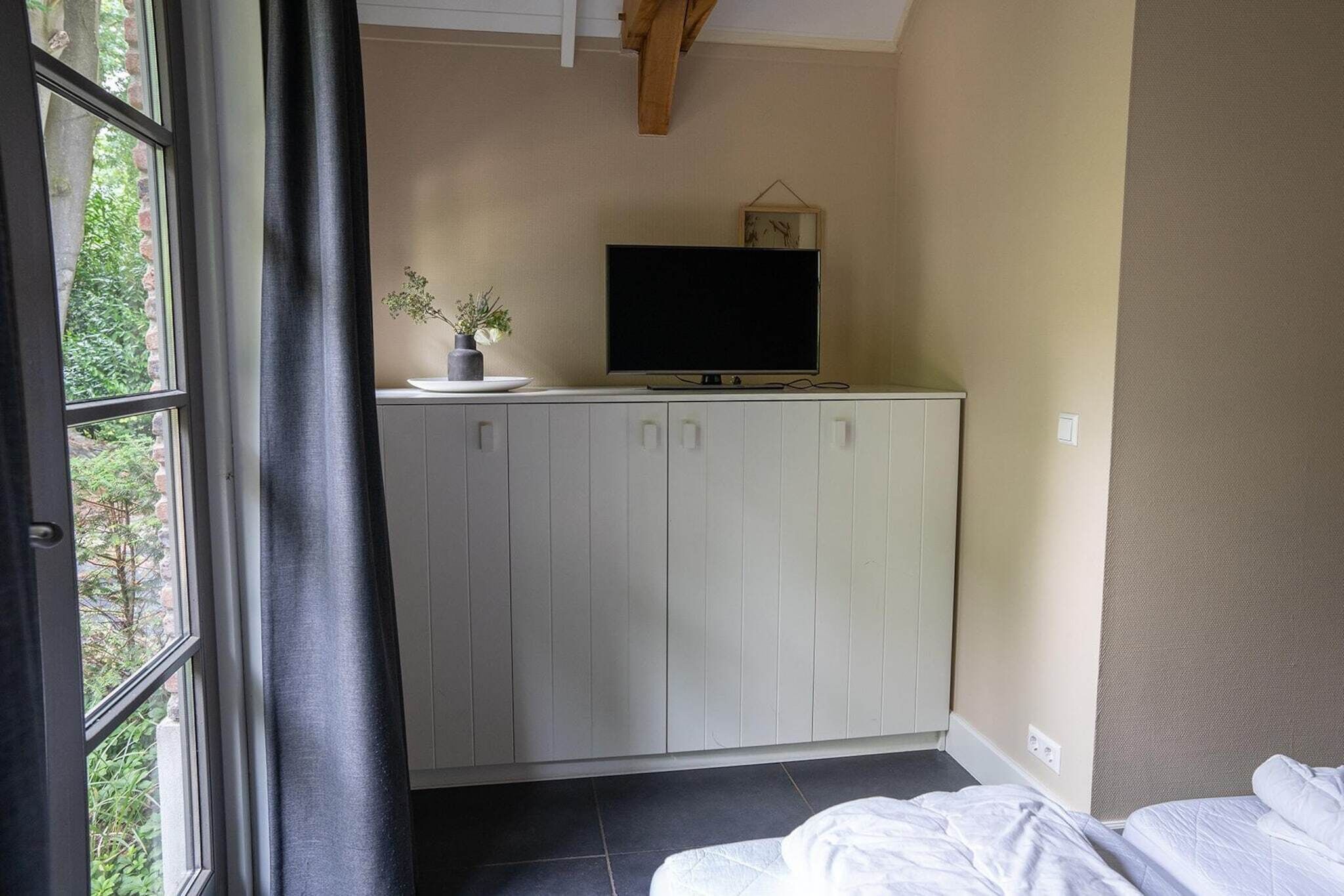 A bedroom with a bed, a TV on a cabinet, and a window with curtains.