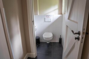 A small, clean bathroom with a toilet, a trash bin, and a wall-mounted flush handle. - Farmhouse in Veluwe with Sauna and Nature Views (Ermelo)