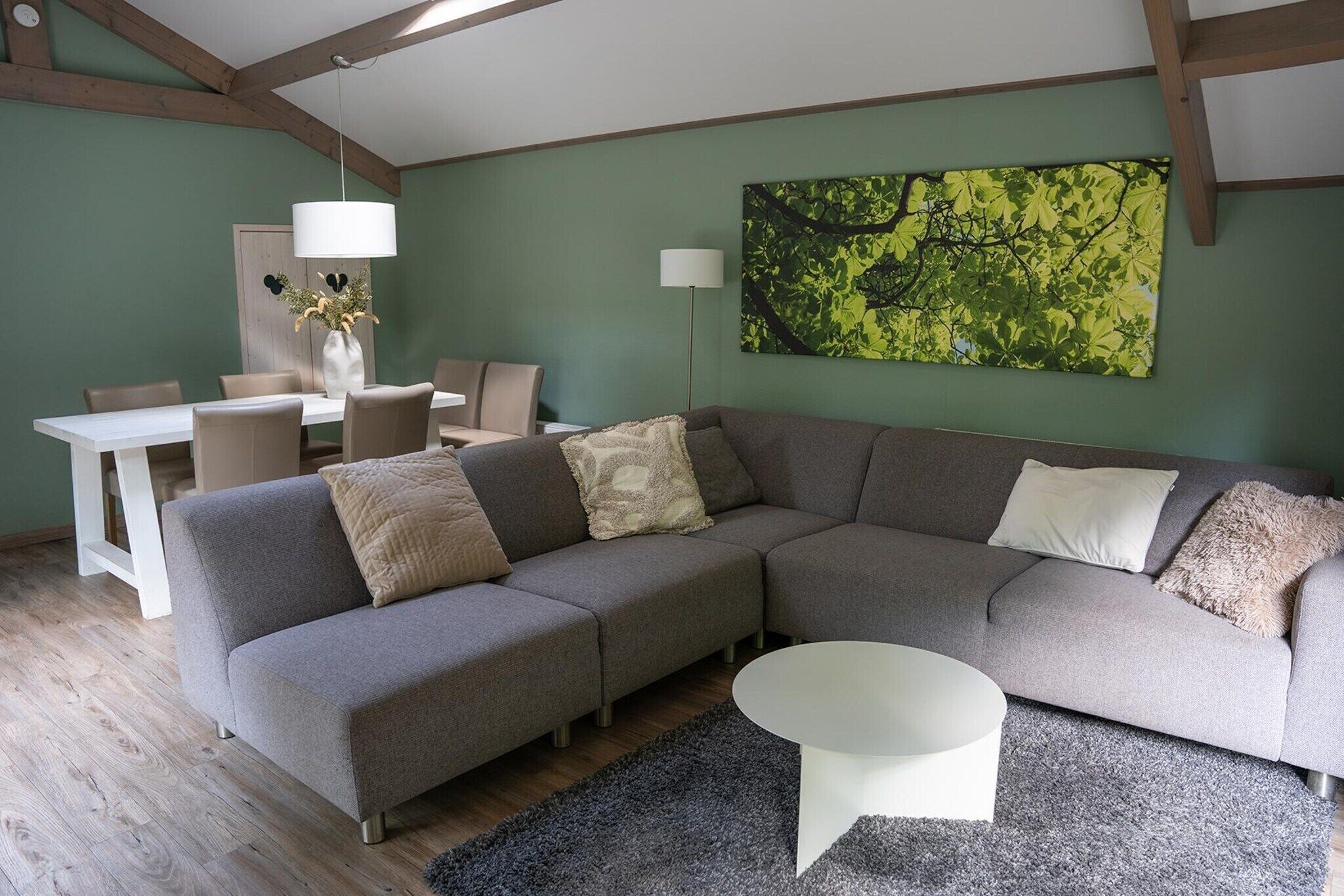 A modern living room with a grey sectional sofa, a white coffee table, and a dining area with a white table and chairs.